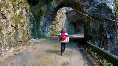 Genç bir fotoğrafçı kız sırt çantasıyla kayalık bir vadide güzel bir dağ yolunda seyahat ediyor. Dağlardaki güzel tüneller ve mağaralar. Dağlarda ve nehirlerde yürüyüş yapmak.