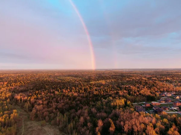 A rainbow over the forest at sunset from a high altitude. Beautiful panoramic landscape of autumn forest and rainbow at sunset from drone
