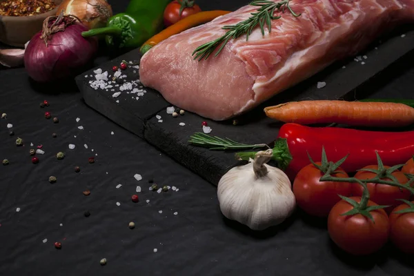 Carne di maiale cruda su un tagliere con rosmarino, verdure e spezie . — Foto Stock