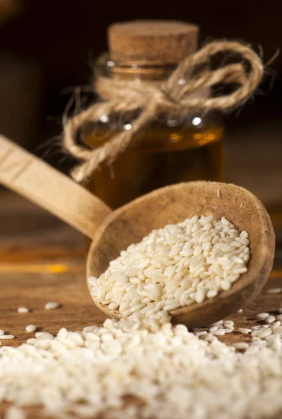 Fresh sesame oil in a glass bottle and seeds in a wooden spoon — Stock Photo, Image