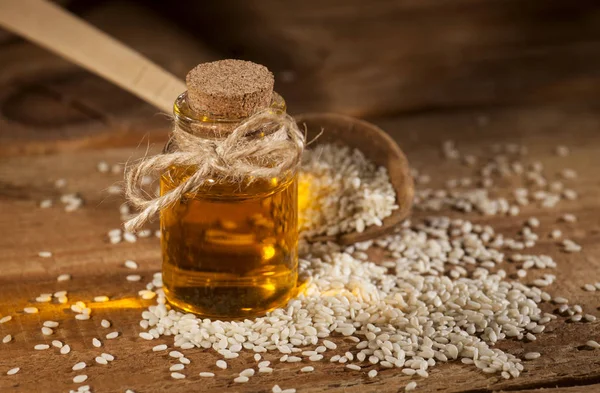 Olio di sesamo fresco in una bottiglia di vetro e semi in un cucchiaio di legno — Foto Stock