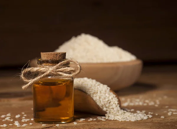 Aceite de sésamo fresco en una botella de vidrio y semillas en un tazón de madera y cuchara —  Fotos de Stock