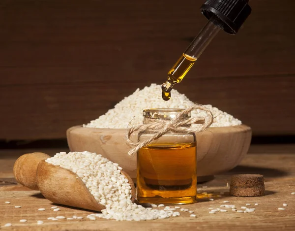 Свежее кунжутное масло в стеклянной бутылке и семена в деревянной миске и ложке — стоковое фото