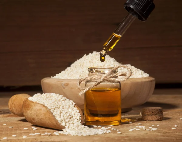 Aceite de sésamo fresco en una botella de vidrio y semillas en un tazón de madera y cuchara —  Fotos de Stock