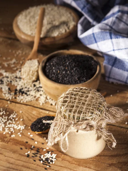 Fresh homemade sesame tahini in a glass jar and seeds in wooden bowls and spoons — Stock Photo, Image