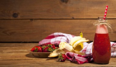 Çilek ve muz smoothie veya milkshake şişe ahşap arka plan üzerinde.