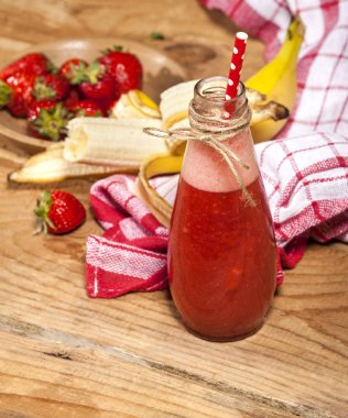 Çilek ve muz smoothie veya milkshake şişe ahşap arka plan üzerinde.