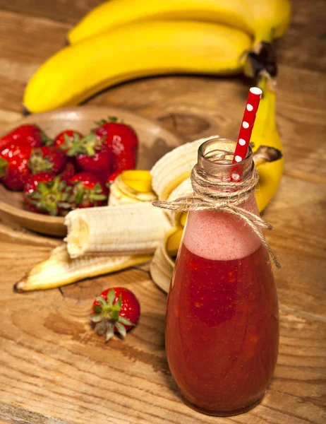 Smoothie van aardbei en banaan of milkshake in fles op houten achtergrond. — Stockfoto