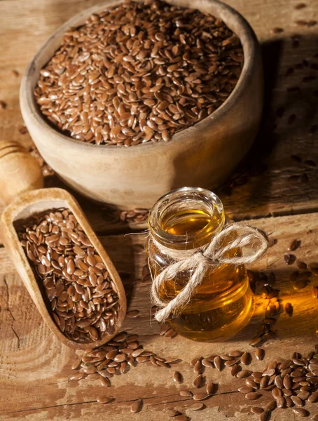 Linseed oil and bowl of linseeds on wooden background — Stock Photo, Image