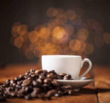 Kahve fincanı ve ahşap masa ve bokeh arka plan üzerinde kahve çekirdekleri