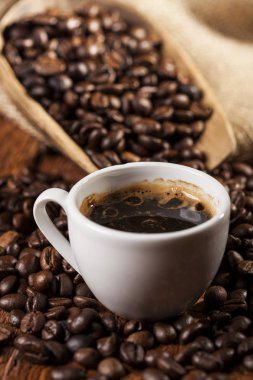 Kahve fincanı ve tahta bir masada kahve çekirdekleri ile çuval. Üstte görüntü.