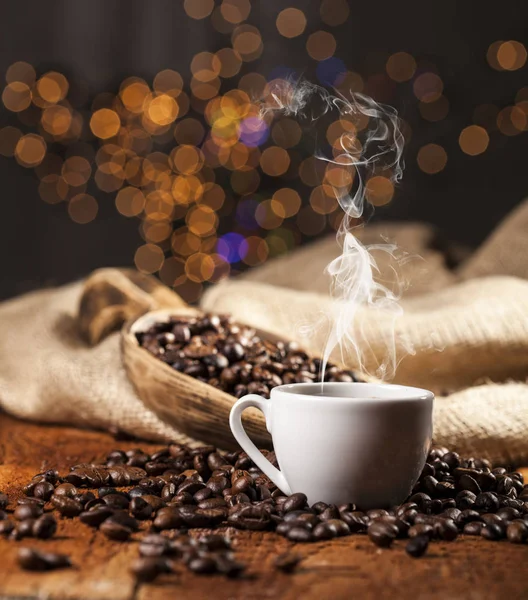 Coffee cup and sack with coffee beans on a wooden table and bokeh background — Stock Photo, Image