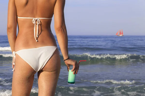 Close up udendørs skud af ung kvinde i hvid bikini med glas kold frisk cocktail solbadning på havet kysten . - Stock-foto