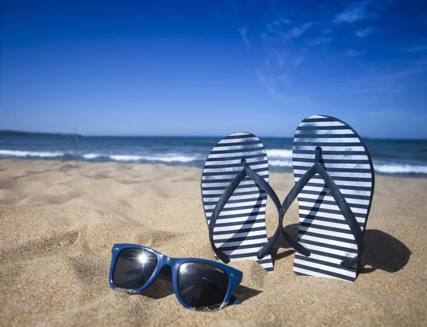 Niebieskie sandały przerzucania flop i okulary przeciwsłoneczne, piaszczystej plaży z niebieskim tle morze i niebo w wakacje. Miejsce — Zdjęcie stockowe