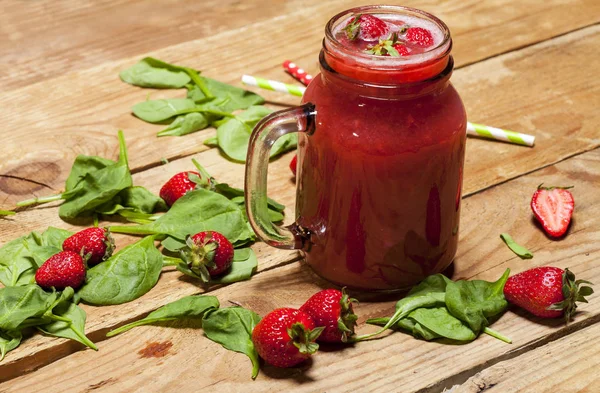 Batido de fresa o batido en un frasco y hojas de espinaca sobre fondo de madera . — Foto de Stock