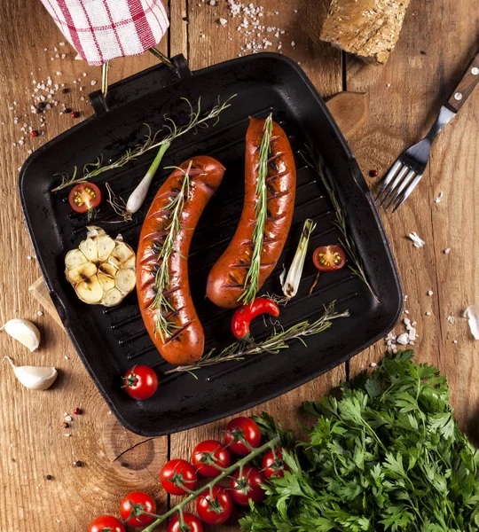 Грильовані ковбаски на сковороді на дерев'яному фоні — стокове фото
