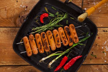 Otlar, baharatlar ve sebzeler tavada kızarmış sosis. Ahşap arka plan üzerinde.