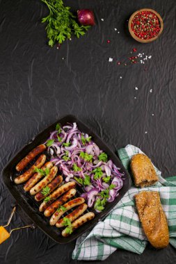 Soğan ve maydanoz siyah arka plan üzerine bir tavada kızarmış sosis