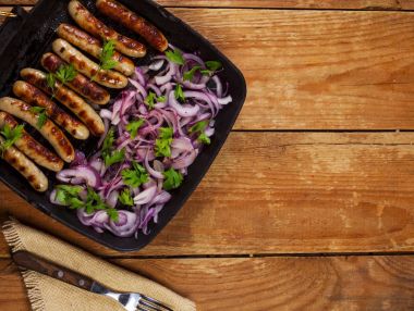 Soğan ve maydanoz ahşap arka plan üzerinde bir tavada kızarmış sosis