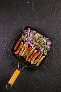 Soğan ve maydanoz siyah arka plan üzerine bir tavada kızarmış sosis