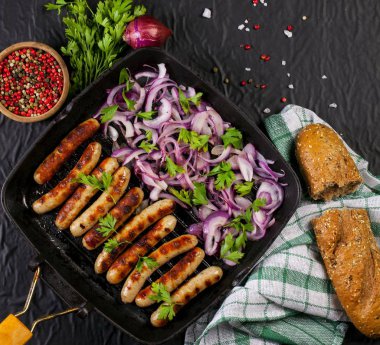 Soğan ve maydanoz siyah arka plan üzerine bir tavada kızarmış sosis