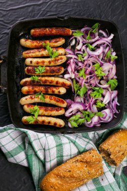 Soğan ve maydanoz siyah arka plan üzerine bir tavada kızarmış sosis