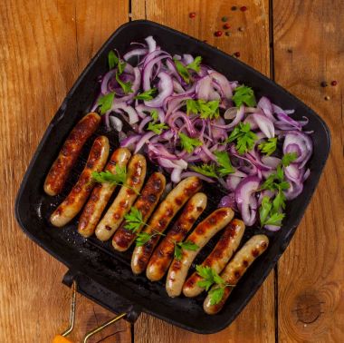 Soğan ve maydanoz ahşap arka plan üzerinde bir tavada kızarmış sosis