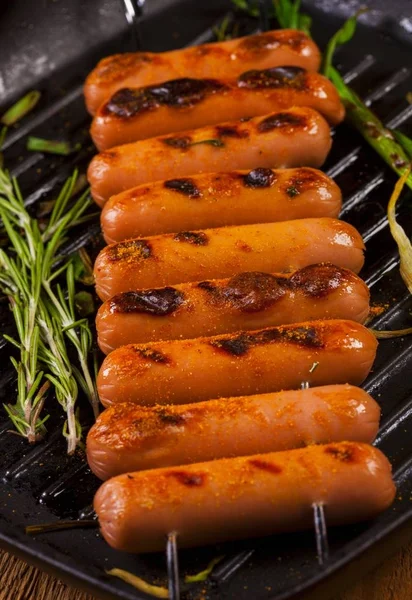 Fried sausages with herbs, spices and vegetables in a pan close up.