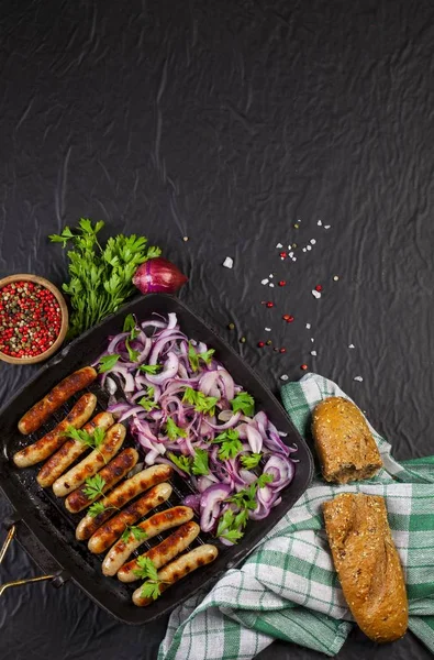 Soğan ve maydanoz siyah arka plan üzerine bir tavada kızarmış sosis