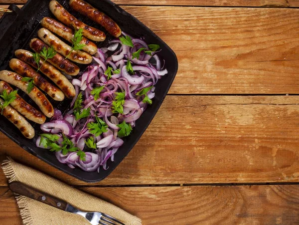 Soğan ve maydanoz ahşap arka plan üzerinde bir tavada kızarmış sosis