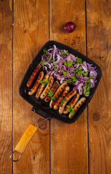 Soğan ve maydanoz ahşap arka plan üzerinde bir tavada kızarmış sosis