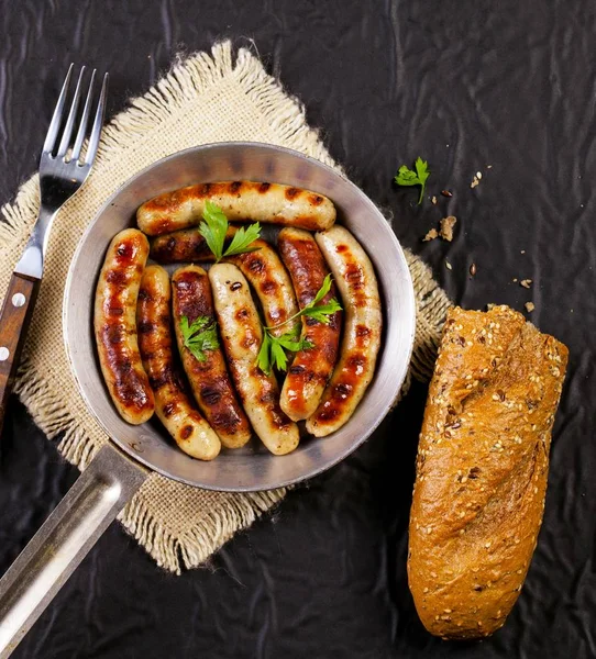 黑底锅里有欧芹、面包和叉子的煎香肠 — 图库照片