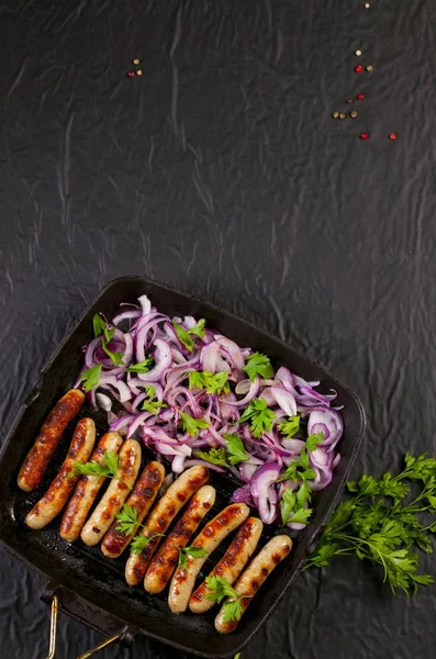 Soğan ve maydanoz siyah arka plan üzerine bir tavada kızarmış sosis