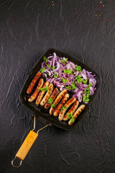 Soğan ve maydanoz siyah arka plan üzerine bir tavada kızarmış sosis