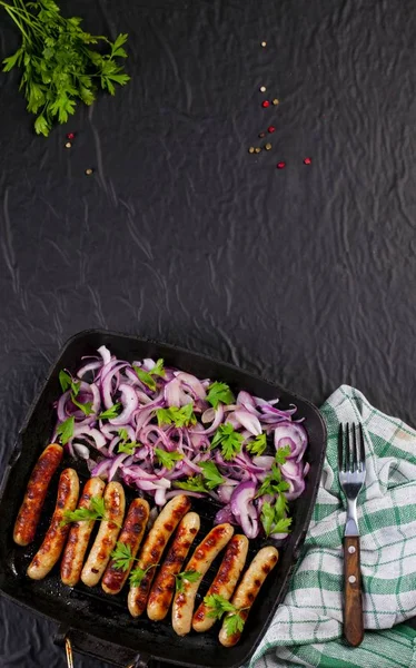 Soğan ve maydanoz siyah arka plan üzerine bir tavada kızarmış sosis