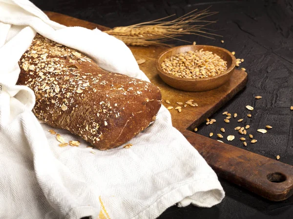 Pane con fiocchi d'avena e grano su un tavolo nero — Foto Stock