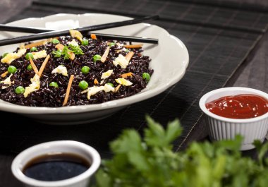 Ahşap arka planda soslu ve çubuklu sebzeli siyah pilav..