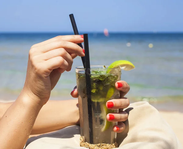 Woman's hands holding glass of fresh mojito cocktail on the beach — Stock Photo, Image