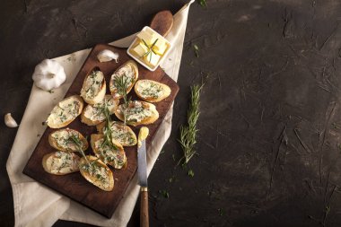 Tereyağlı, zeytinli, sarımsaklı ve otlu dilimlenmiş geleneksel tost ekmeği kesme tahtasında, peçetede ve karanlık masada.