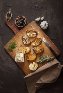 Tereyağlı, zeytinli, sarımsaklı ve otlu dilimlenmiş geleneksel tost ekmeği kesme tahtasında, peçetede ve karanlık masada.
