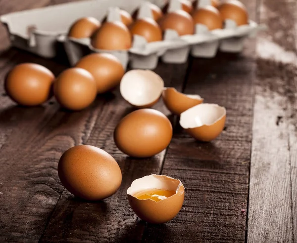 상자 안에 들어 있는 갈색의 달걀 과 시골 식탁에 있는 노른자와 깨어진 달걀. — 스톡 사진