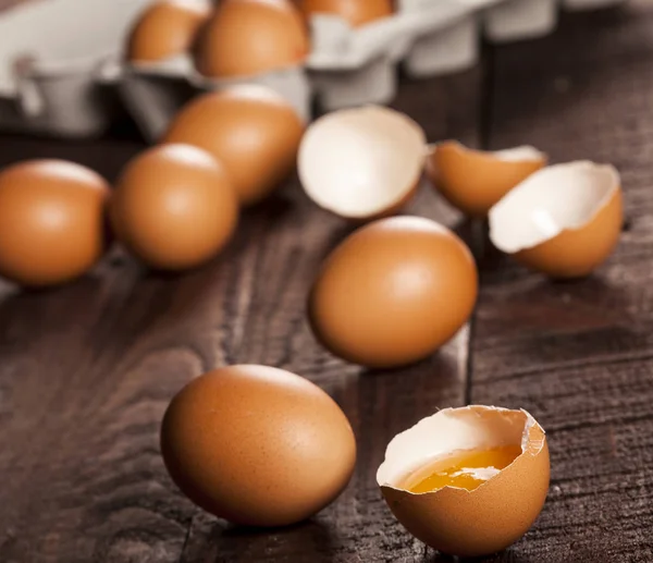 Bruine eieren in een doos en gebroken ei met dooier op rustieke tafel. — Stockfoto