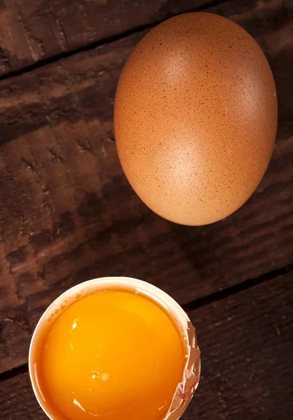 Brown egg and broken egg with yolk on rustic table.