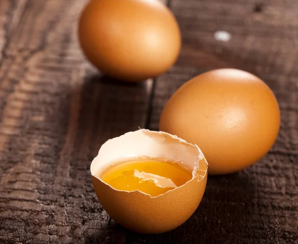 Bruine eieren en gebroken ei met dooier op rustieke tafel. — Stockfoto