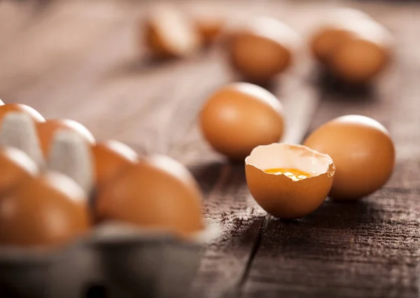 Bruine eieren in een doos en gebroken ei met dooier op rustieke tafel. — Stockfoto