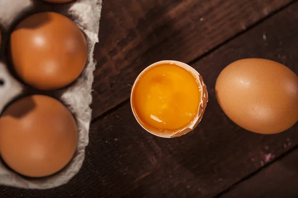 Bruine eieren in een doos en gebroken ei met dooier op rustieke tafel. — Stockfoto