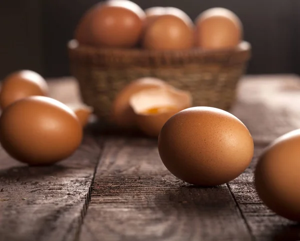 Bruine eieren in een mand en gebroken ei met dooier op rustieke tafel. — Stockfoto