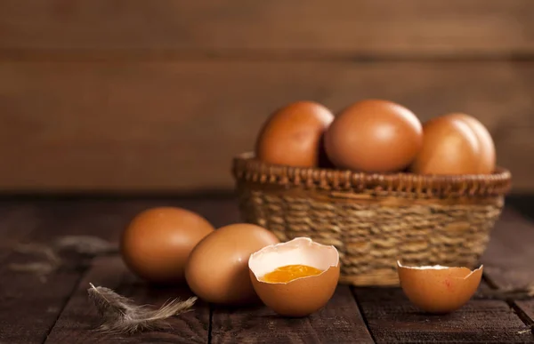 Bruine eieren in een mand en gebroken ei met dooier op rustieke tafel. — Stockfoto