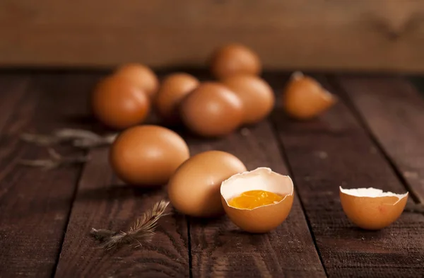 Brown eggs and broken egg with yolk on rustic table.