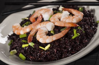 Karidesli siyah pirinç ve siyah arka planda yeşil soğan..